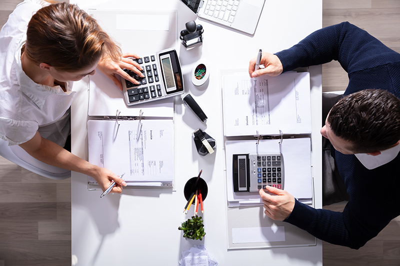 Male And Female Business people Calculating Invoice
